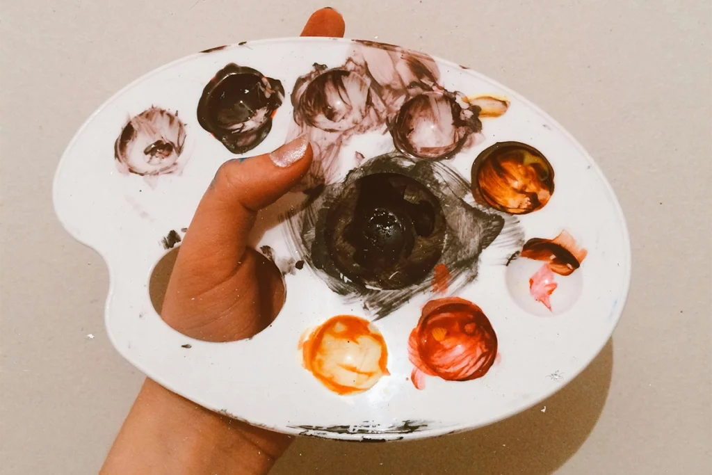 Mano sosteniendo una paleta de pintura con varios colores mezclados.