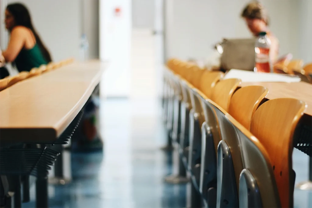Aula vacía con filas de mesas y sillas en perspectiva.