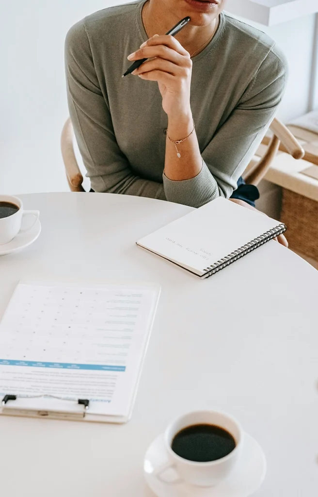 Mujer tomando notas con un bolígrafo junto a una taza de café.